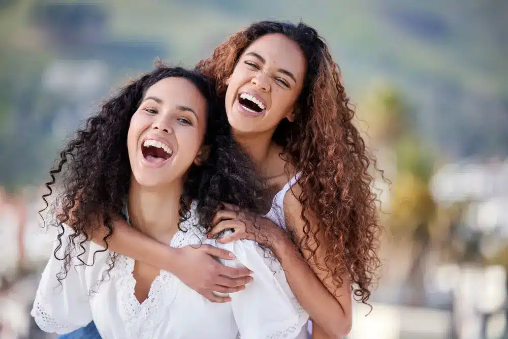 Two women laughing together with bright, confident smiles and healthy teeth after Dental Implant